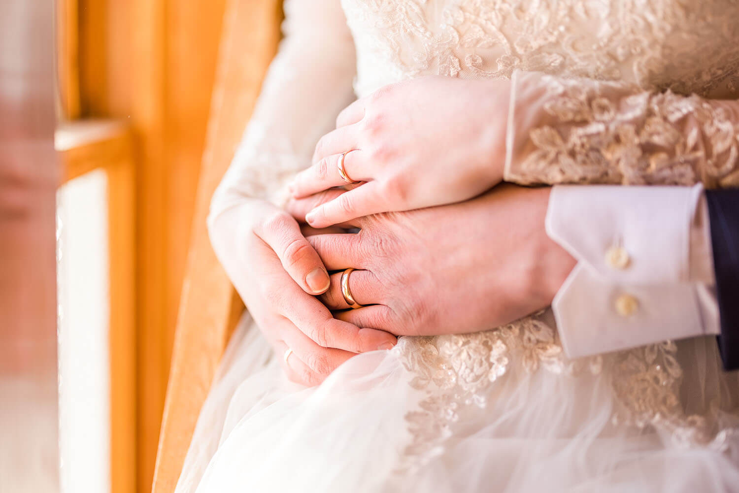 close up of a bride and groom's hands intertwined wearing matching gold wedding ring bands