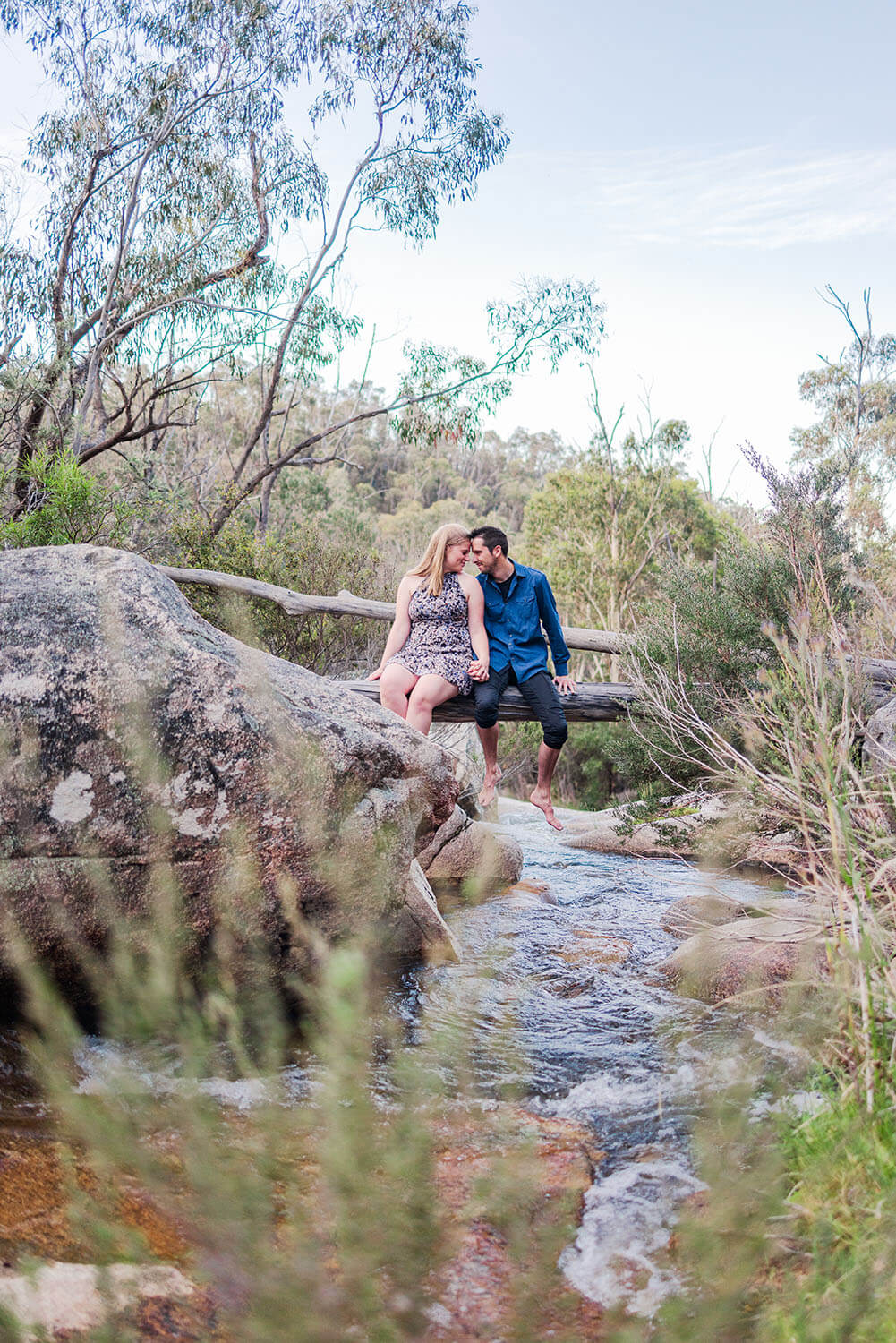 man and woman sitting on a log over hanging a creek