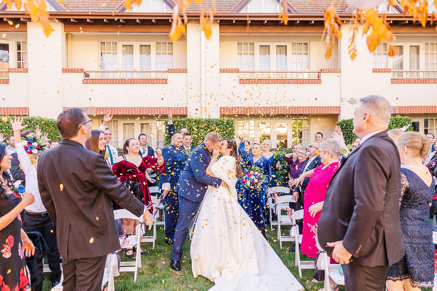 Bride and Groom kissing while guests throw yellow leaves in the air