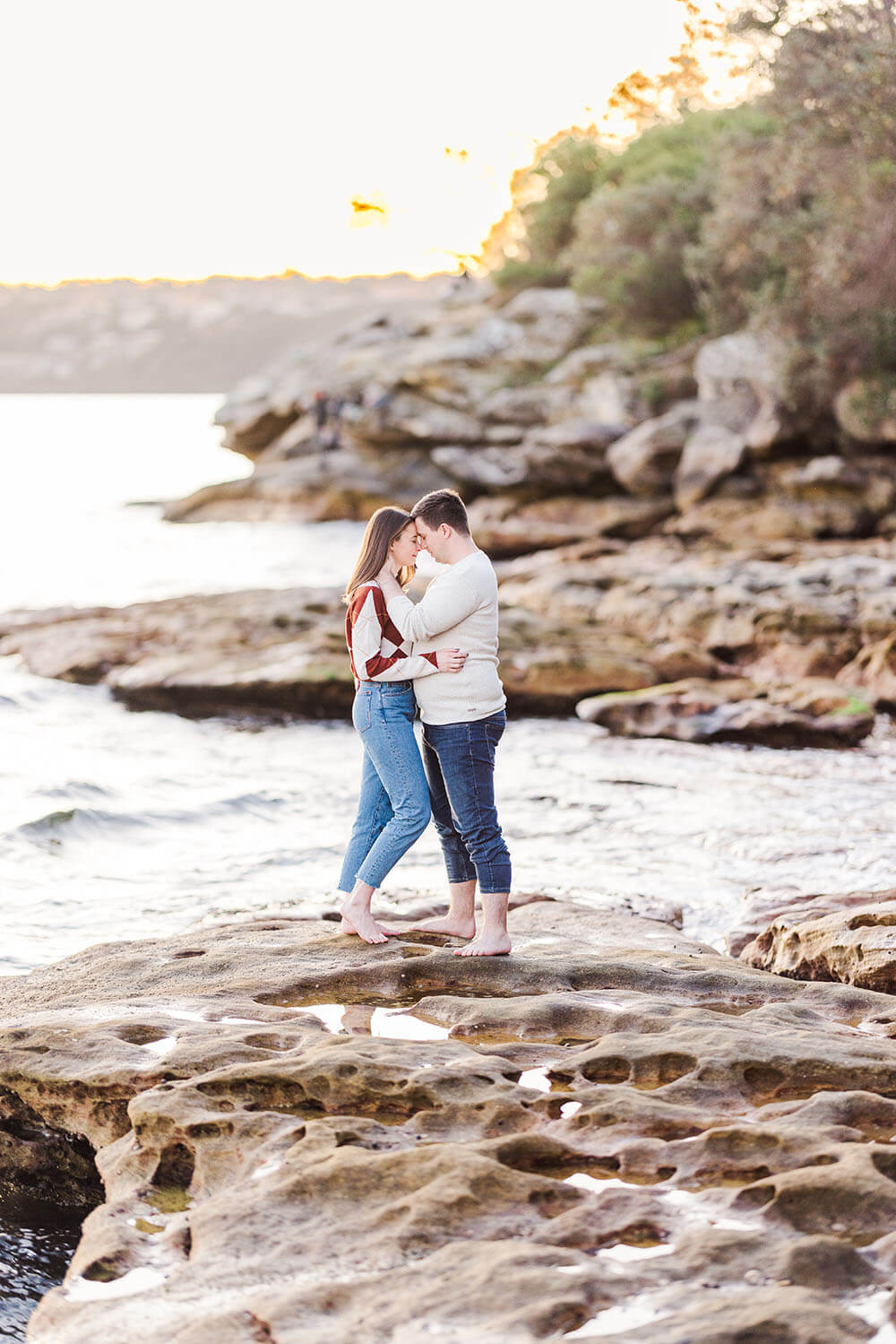 couple standing on the rocks by and ocean with their foreheads together in a loving embrance