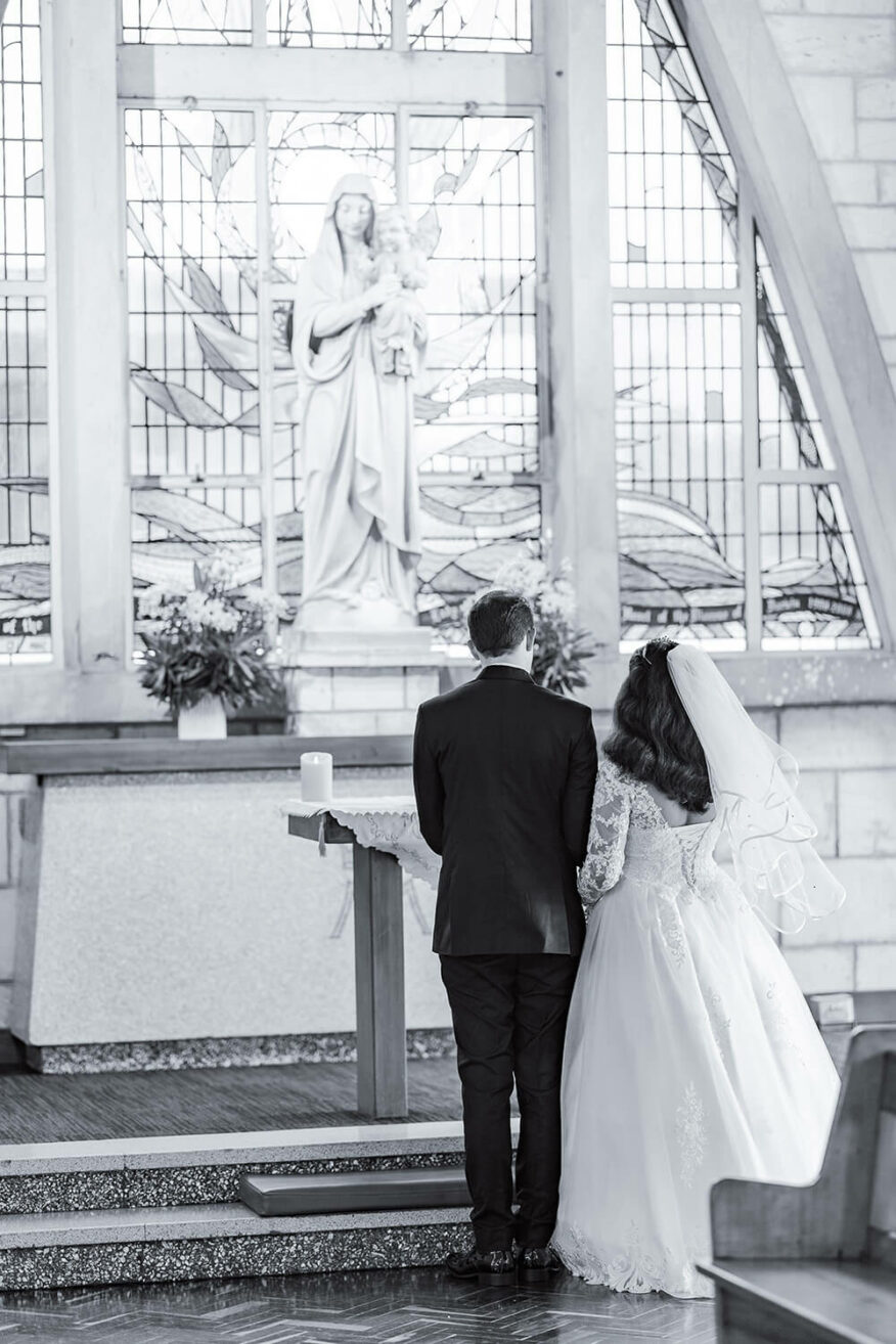 catholic bride and groom praying to a statue of mary on their wedding day