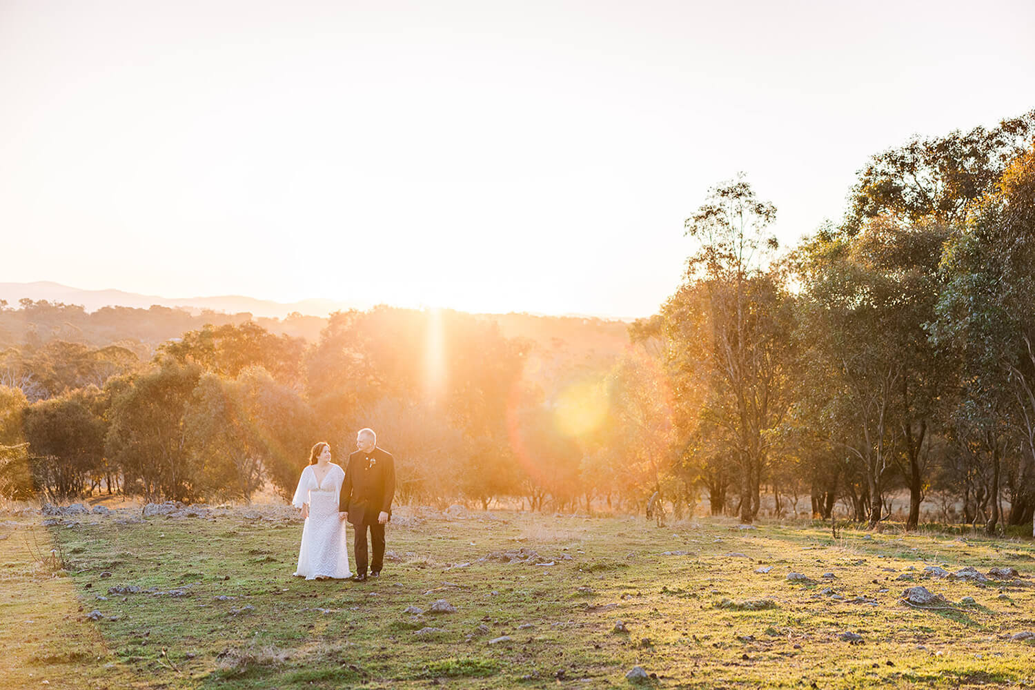 a bride and groom walking in a sunset view over the brindabella range at Gold Creek Station