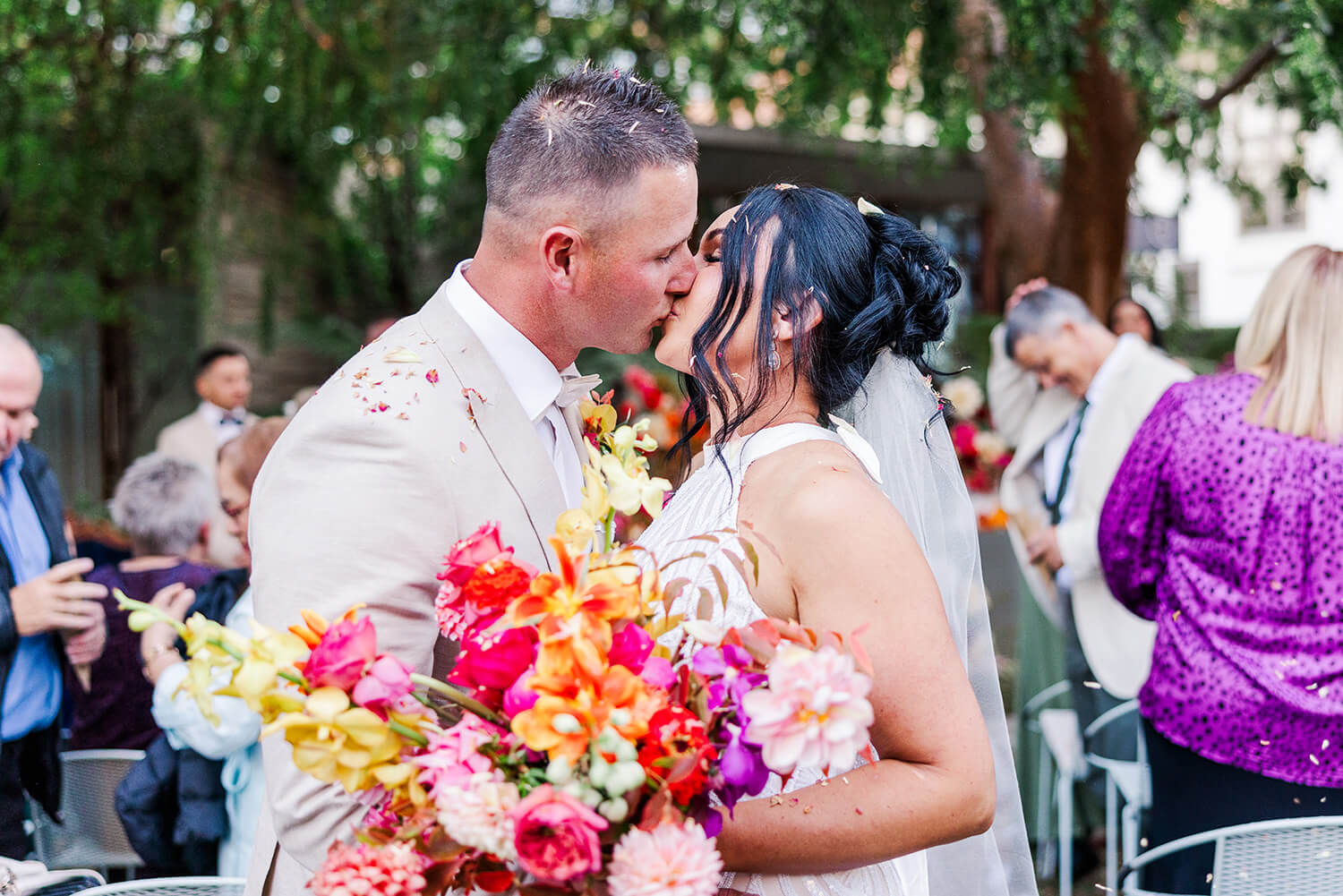 bride and groom kiss behind a bunch of colourful flowers