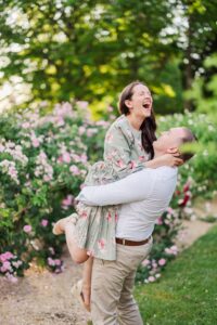 man in a white shirt lifting a woman in a green flower dress up in the air and she screams with joy